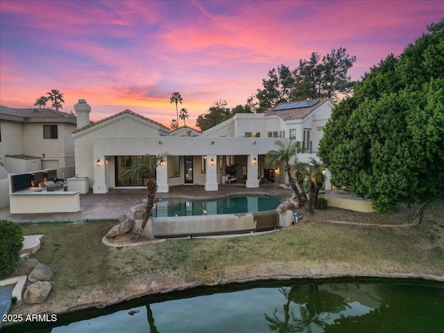 back of house at dusk with a patio area, a lawn, an outdoor pool, and exterior kitchen