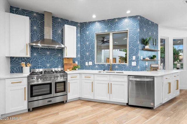 kitchen with a sink, wall chimney range hood, stainless steel appliances, and light countertops