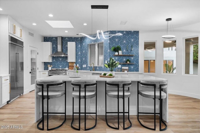 kitchen featuring wall chimney exhaust hood, high end appliances, hanging light fixtures, white cabinets, and a kitchen breakfast bar