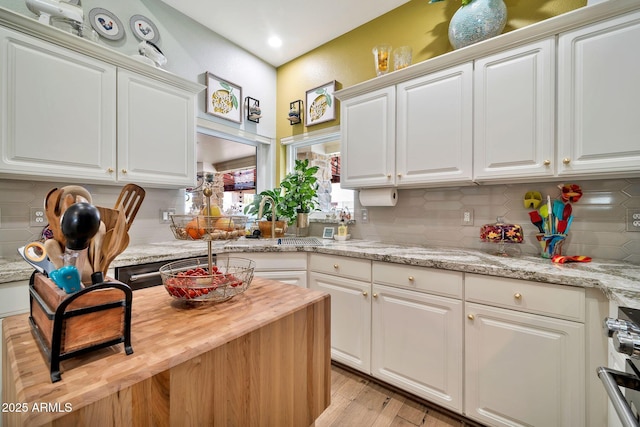 kitchen featuring white cabinetry, backsplash, light stone counters, and light hardwood / wood-style flooring