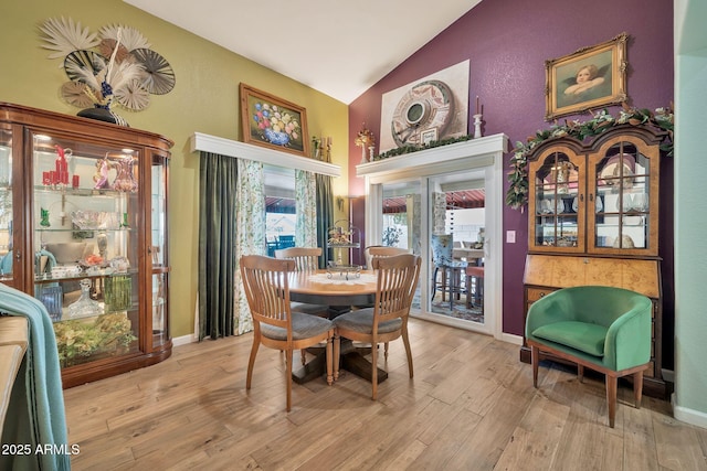 dining space featuring high vaulted ceiling and light hardwood / wood-style floors