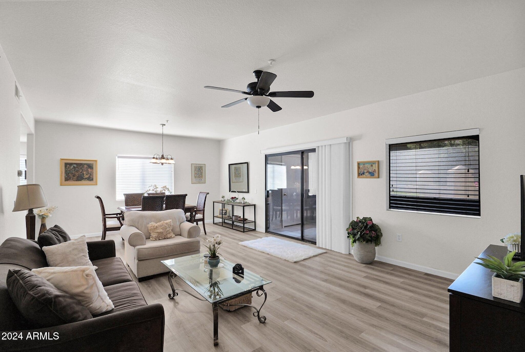 living room with ceiling fan with notable chandelier and light hardwood / wood-style flooring