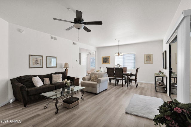 living room featuring ceiling fan with notable chandelier and light hardwood / wood-style flooring