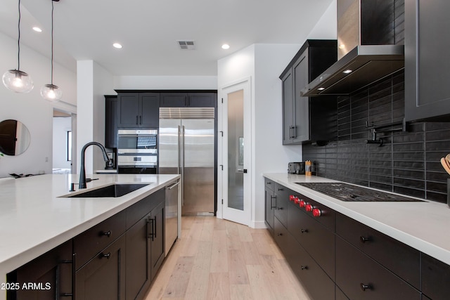 kitchen with visible vents, a sink, light countertops, stainless steel appliances, and wall chimney exhaust hood