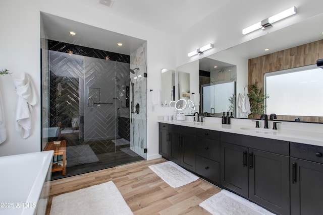 bathroom featuring double vanity, a sink, wood finished floors, and a shower stall