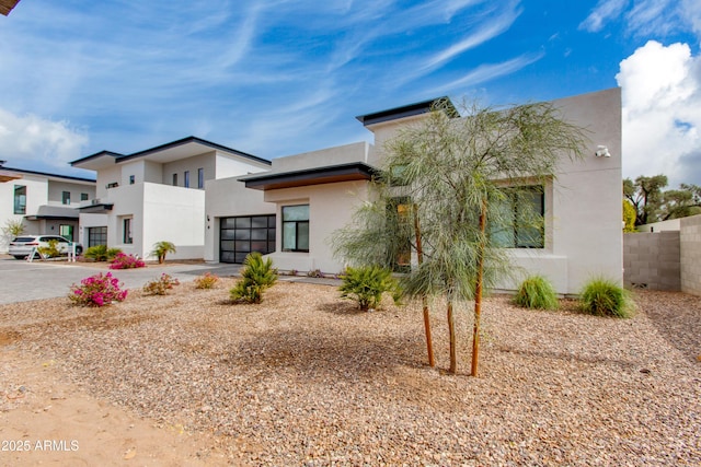 modern home with fence, an attached garage, driveway, and stucco siding