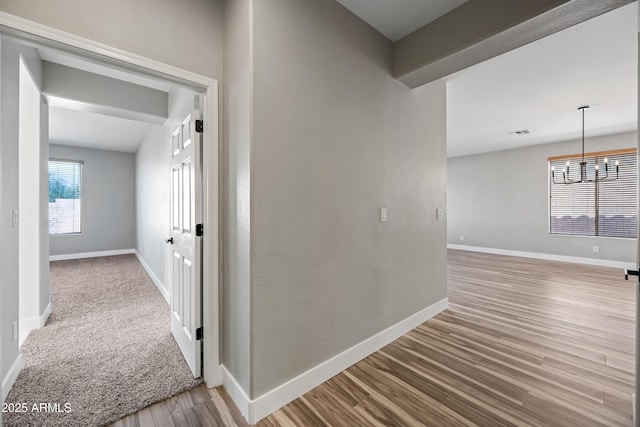 hallway featuring an inviting chandelier, wood finished floors, and baseboards