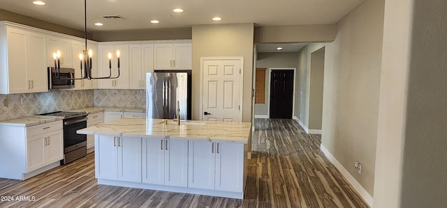 kitchen with white cabinetry, light stone counters, appliances with stainless steel finishes, and a center island with sink