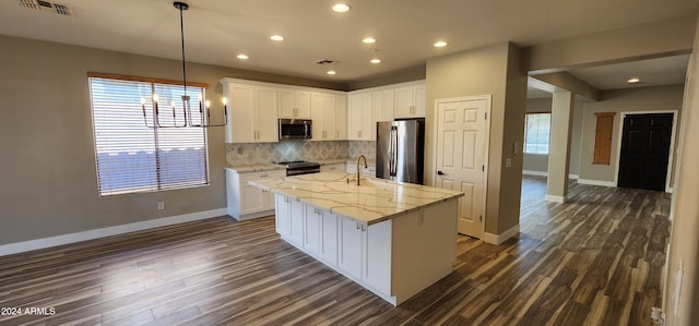 kitchen featuring white cabinetry, stainless steel appliances, light stone countertops, and an island with sink