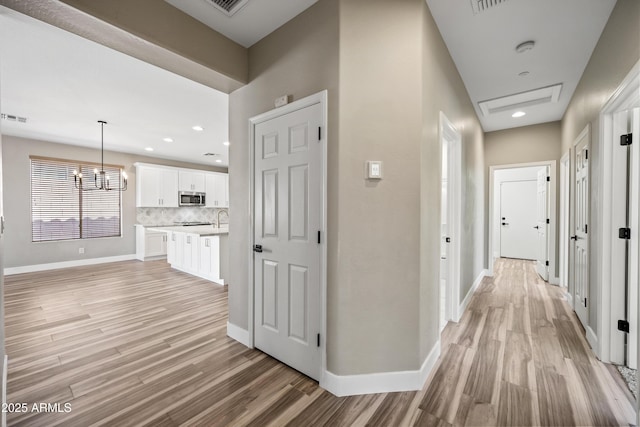 hallway featuring visible vents, light wood-style floors, a notable chandelier, and baseboards