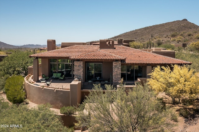 rear view of house featuring cooling unit, a mountain view, a tile roof, stone siding, and a patio area