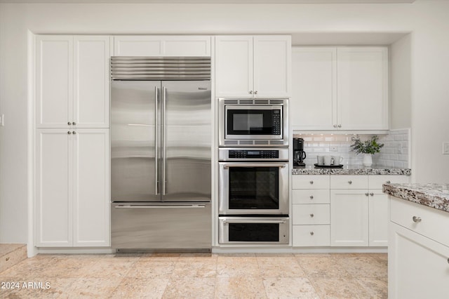 kitchen featuring built in appliances, white cabinets, backsplash, and light tile floors