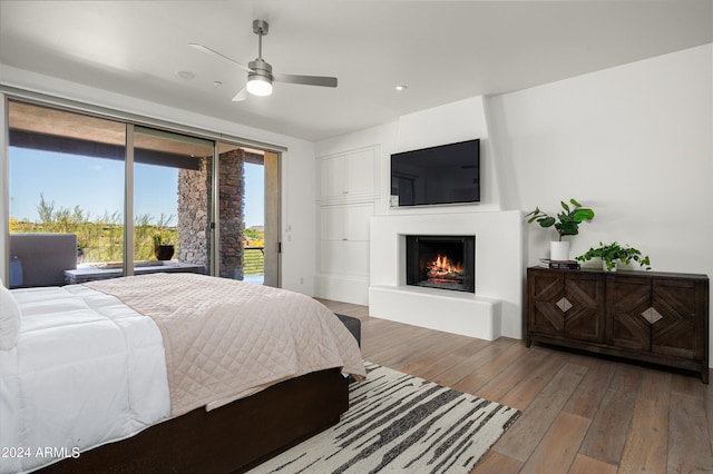 bedroom featuring a warm lit fireplace, a ceiling fan, access to exterior, floor to ceiling windows, and hardwood / wood-style floors