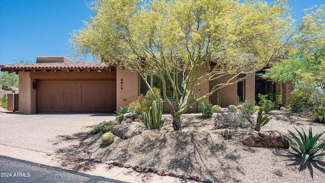 adobe home featuring an attached garage, driveway, a tile roof, and stucco siding