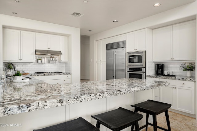 kitchen with built in appliances, tasteful backsplash, and a kitchen bar