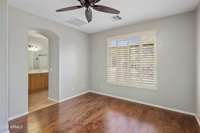 empty room featuring visible vents, a ceiling fan, arched walkways, and hardwood / wood-style floors
