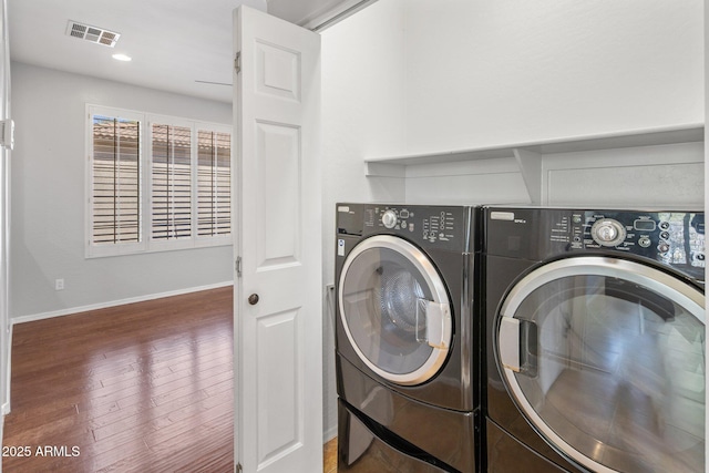 clothes washing area featuring laundry area, visible vents, washing machine and dryer, wood finished floors, and baseboards