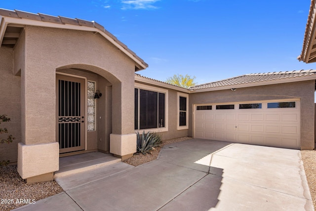 doorway to property with a garage, stucco siding, concrete driveway, and a tile roof