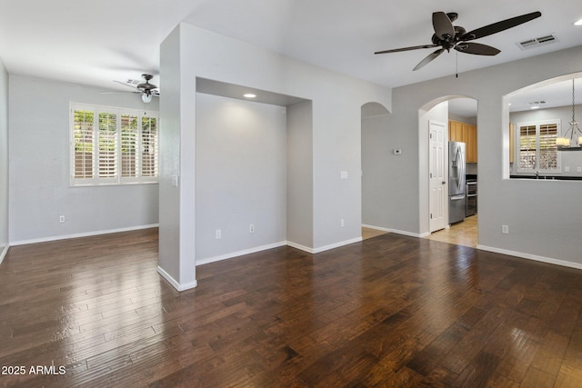 unfurnished living room with visible vents, hardwood / wood-style floors, baseboards, arched walkways, and a ceiling fan