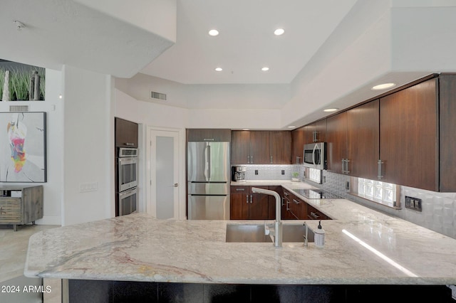 kitchen featuring kitchen peninsula, appliances with stainless steel finishes, light stone countertops, and sink