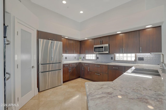 kitchen with sink, stainless steel appliances, light stone counters, kitchen peninsula, and dark brown cabinets