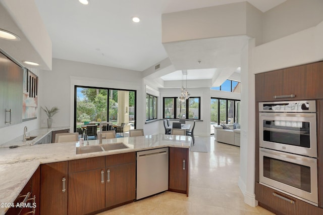 kitchen with light stone countertops, kitchen peninsula, appliances with stainless steel finishes, and an inviting chandelier