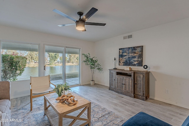 living room featuring ceiling fan, a water view, and light hardwood / wood-style floors