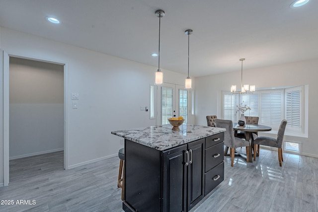 kitchen with decorative light fixtures, light stone countertops, a kitchen island, and light wood-type flooring