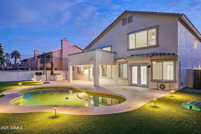 back house at dusk featuring french doors, a patio area, a fenced in pool, and a yard