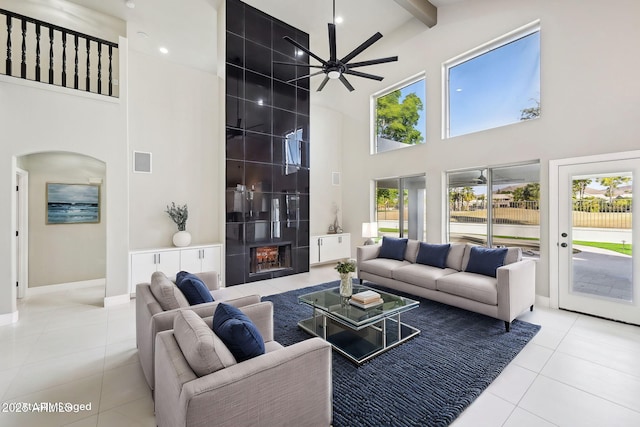 living room with a wealth of natural light, a high ceiling, ceiling fan, light tile patterned flooring, and beamed ceiling