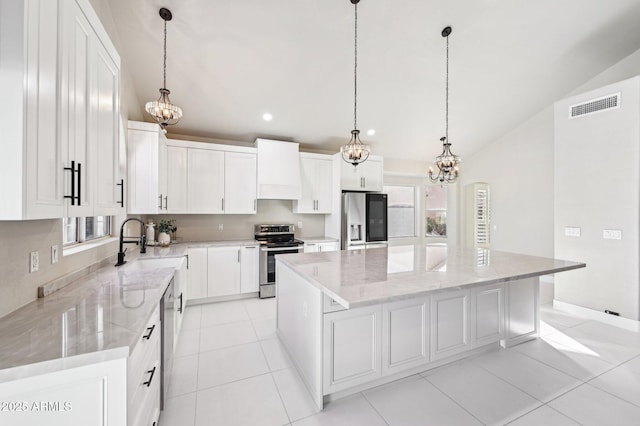 kitchen with hanging light fixtures, stainless steel appliances, wall chimney range hood, a kitchen island, and white cabinetry