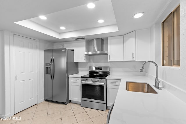 kitchen featuring a raised ceiling, appliances with stainless steel finishes, white cabinets, a sink, and wall chimney range hood