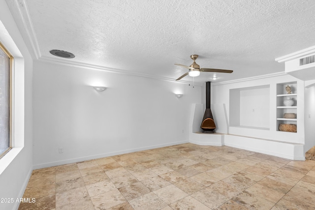 spare room with ceiling fan, a textured ceiling, visible vents, built in features, and a wood stove