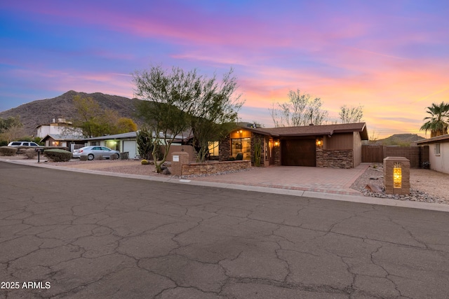 mid-century modern home featuring decorative driveway, an attached garage, fence, a mountain view, and stone siding