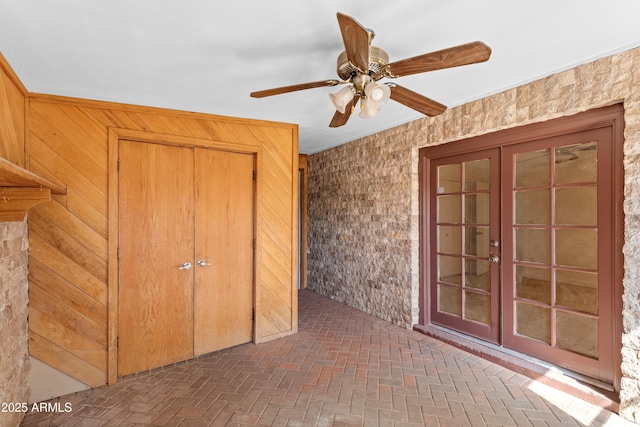 interior space featuring ceiling fan, french doors, brick floor, and wooden walls