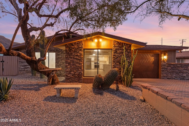 mid-century modern home with a garage, stone siding, and decorative driveway