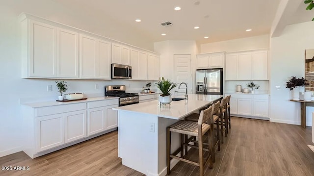 23244 W Tamarisk Ave, Buckeye, AZ 85326 - kitchen featuring stainless steel appliances, light wood finished floors, a center island with sink, a kitchen breakfast bar, and white cabinets