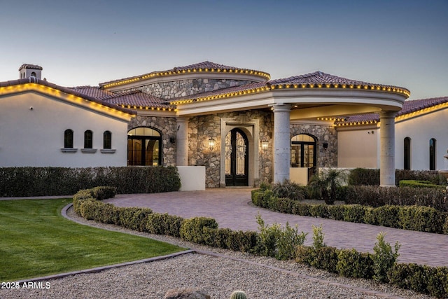 mediterranean / spanish-style home featuring stone siding, french doors, a tile roof, and a front lawn