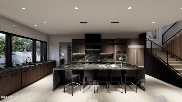 kitchen featuring light wood-type flooring, dark stone counters, a spacious island, and decorative light fixtures