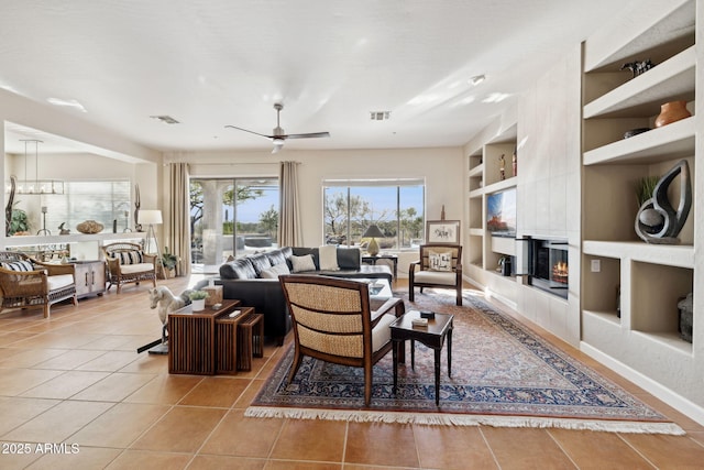 living room with tile patterned flooring, ceiling fan with notable chandelier, a fireplace, and built in shelves