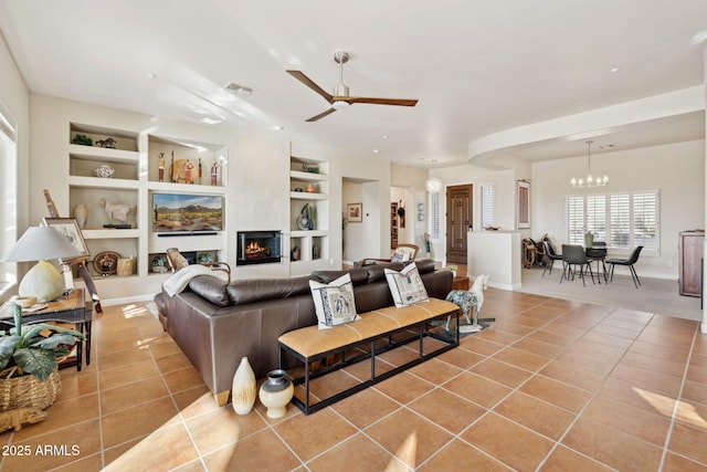 living room featuring light tile patterned flooring, ceiling fan with notable chandelier, and built in shelves