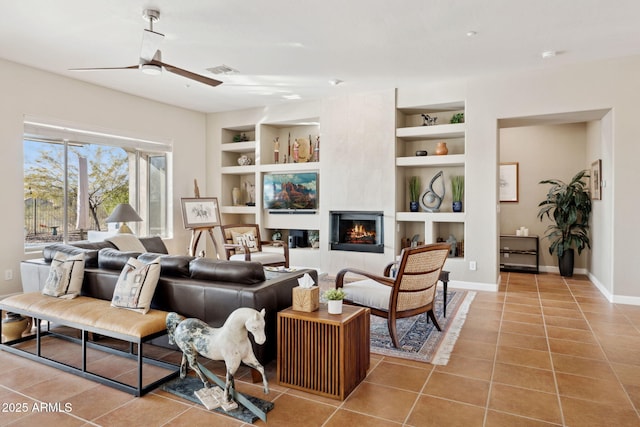 tiled living room with built in shelves, a large fireplace, and ceiling fan