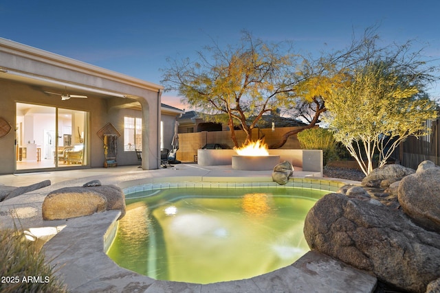 pool at dusk with a patio, ceiling fan, and an outdoor fire pit