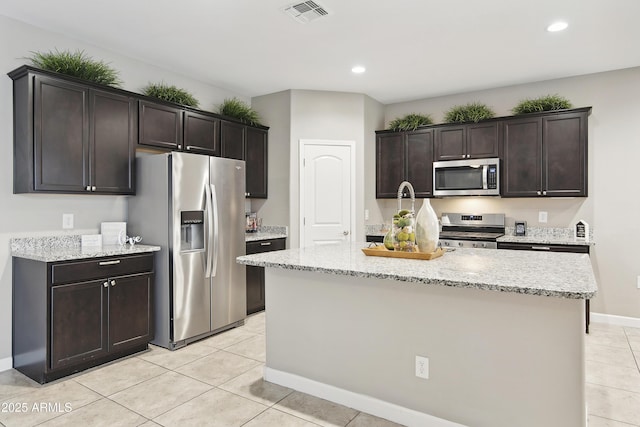 30776 W Earll Dr, Buckeye, AZ 85396 - kitchen featuring appliances with stainless steel finishes, light tile patterned floors, dark brown cabinets, light stone counters, and recessed lighting