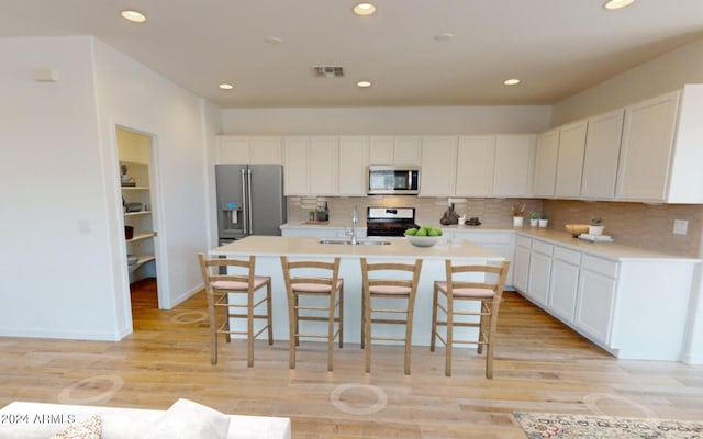 kitchen featuring a sink, a breakfast bar area, stainless steel appliances, white cabinetry, and visible vents