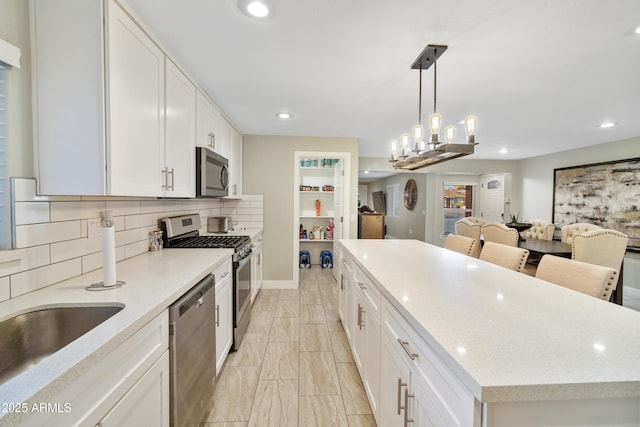 kitchen featuring appliances with stainless steel finishes, white cabinetry, tasteful backsplash, a kitchen island, and decorative light fixtures