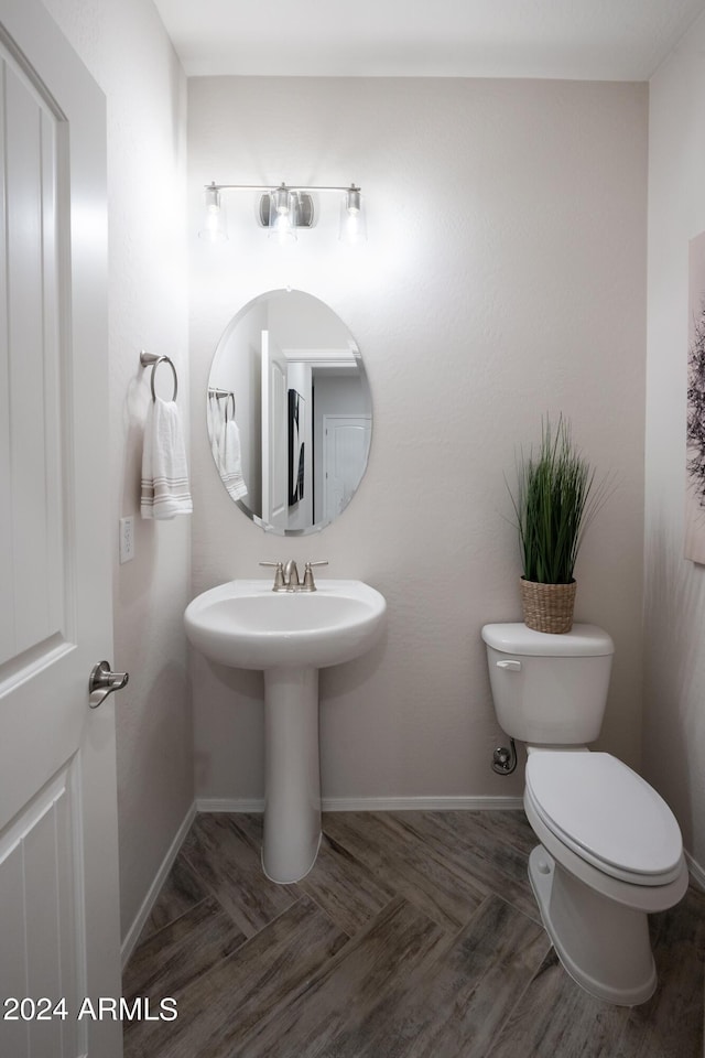 half bathroom with a sink, toilet, baseboards, and wood finished floors