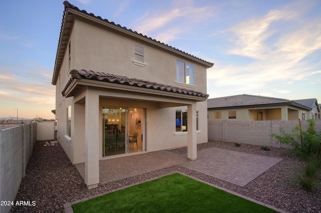 back of house at dusk featuring a patio area, a fenced backyard, and stucco siding