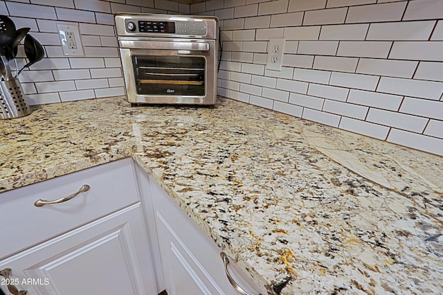 interior details featuring tasteful backsplash, stainless steel oven, white cabinets, and light stone counters