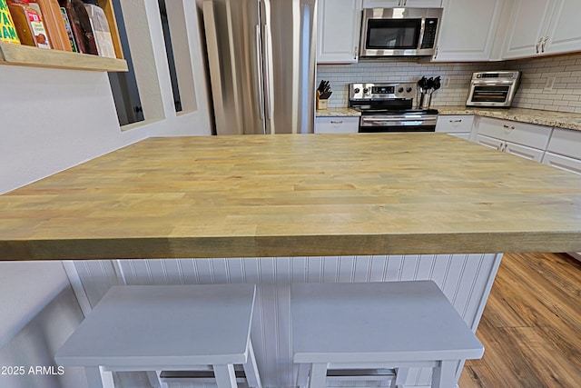 kitchen featuring tasteful backsplash, light stone countertops, appliances with stainless steel finishes, and white cabinets